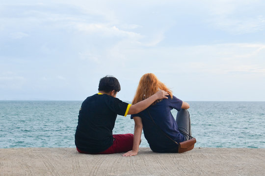 Friend Or Couple Lover Siting On Mortar. Man Put One Arm Around Another Is Shoulder With Women Is Gold Hair. Couple Looking At The Sea. Comforting, Sweet Couple, Travel, Friend Forever Concept.