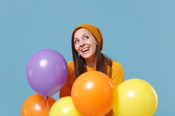 Fototapeta na wymiar Pensive young woman girl in sweater and hat posing isolated on blue background. Birthday holiday party, people emotions concept. Mock up copy space. Celebrating hold colorful air balloons looking up.