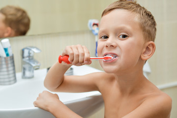 child brushes his teeth with toothbrush in bathroom