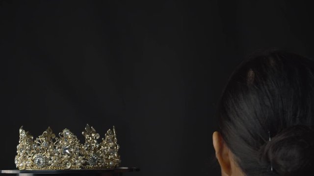 Beauty pageant queen or bride places a diamond, pearl and silver crown on her head - black background