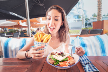 Cheerful tourist girl tries Greek cuisine at a local restaurant. On the table traditional salad Horiatiki and Gyros in Pita