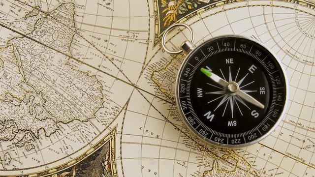 Disorientated spinning compass against map background closeup footage