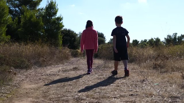 Young kids brother and sister walking together on a path. Slow-motion gimbal shot.
