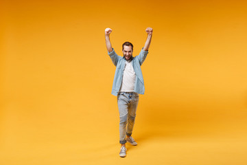Joyful young bearded man in casual blue shirt posing isolated on yellow orange background studio...