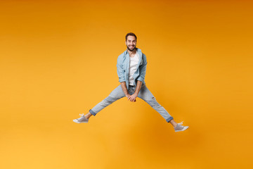 Fototapeta na wymiar Smiling young bearded man in casual blue shirt posing isolated on yellow orange wall background, studio portrait. People sincere emotions lifestyle concept. Mock up copy space. Jumping spreading legs.