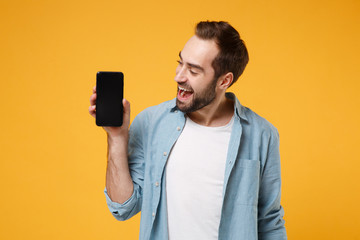 Cheerful young man in casual blue shirt posing isolated on yellow orange wall background, studio...