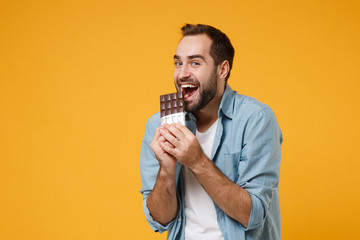 Cheerful young man in casual blue shirt posing isolated on yellow orange wall background, studio...