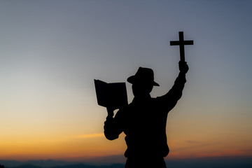 Silhouette of a young Christian man who is praying on the holy cell in the Bible and raising a...