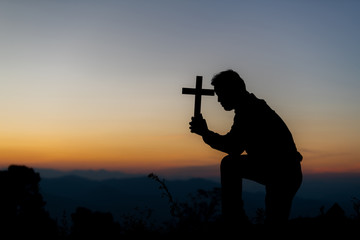 Silhouette of a young Christian praying to God at sunrise in the background of Christianity concept