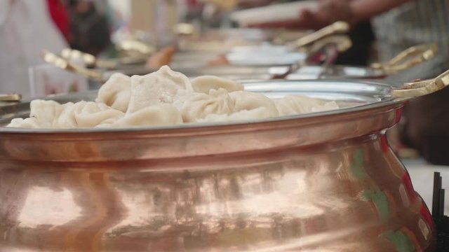 The row of casseroles with pelmeni, rice and other asian food. Pelmeni on foreground are focused.