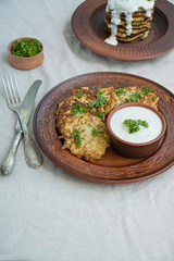 Zucchini fritters. Vegetarian zucchini pancakes with fresh herbs and sour cream. A stack of pancakes. Dining table. Balance healthy food. Light background.