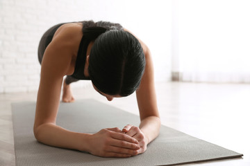 Young woman practicing forearm plank asana in yoga studio. Phalankasana pose variation