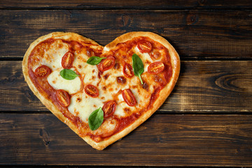 Delicious heart shaped Italian pizza on wooden background