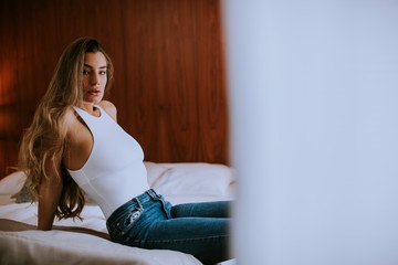 Young woman in stylish jeans pants sitting on bed at home