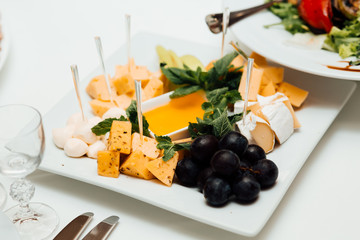 Cheese, grapes and honey on the table. Delicious dishes on the table in the restaurant. Sliced cheese with honey on a white plate. Cheese. Food. Festive table with dishes. Dish.