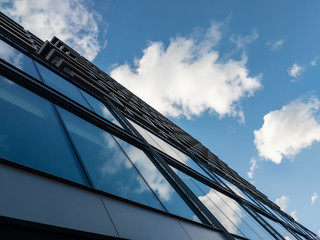 Fototapeta na wymiar Looking up at modern glass building with blue sky and clouds
