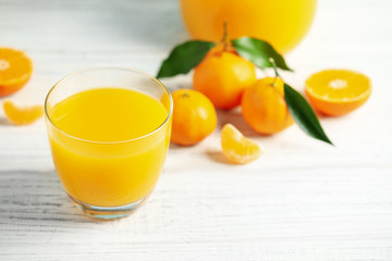 Glass of fresh tangerine juice and fruits on white wooden table