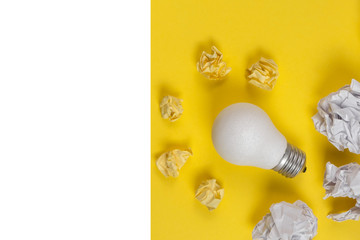 Creativity inspiration, great business idea concept with white light bulb and paper crumpled ball on yellow background. Flat lay, top view, copy space