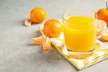 Glass of fresh tangerine juice and fruits on light grey table. Space for text