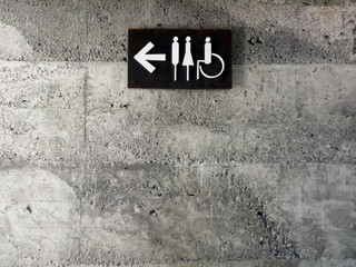 modern public toilet sign on the cement wall. Toilet icon sign on concrete wall . mens and womens disabled restroom signage with arrow made from steel plate on grey concrete wall.