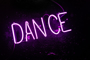 Purple neon light creating the word "DANCE" on a black wall in a disco or night club