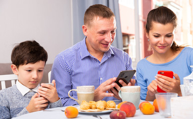 Obraz na płótnie Canvas Parents and teen son using phones at kitchen