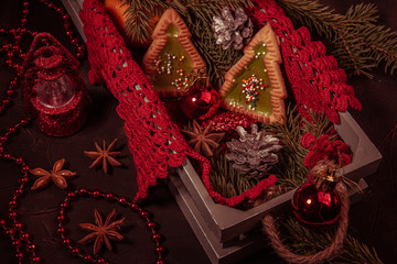 This Christmas dark red background: beautiful cookies in the form of Christmas trees, fir twigs, Christmas decorations, beads, lantern, cones, tangerine. The concept of Christmas and new year holidays