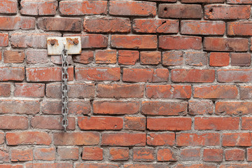 An old wall with exposed red bricks and a metal chain bolted on