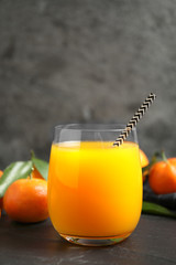 Glass of fresh tangerine juice and fruits on black table