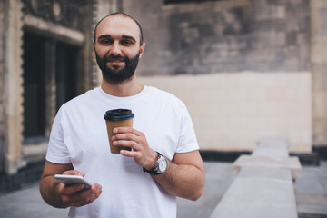 Cheerful man with disposable cup and smartphone looking at camera