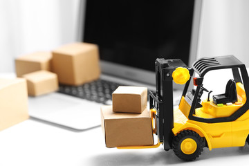 Toy forklift with boxes near laptop on table. Logistics and wholesale concept