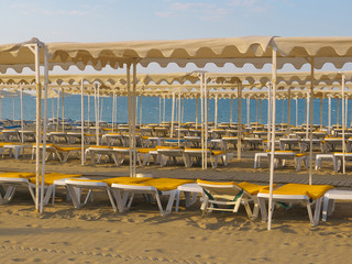 Plastic white chaise lounges on empty beach after a hot season. Leisure or travel concept. White plastic sunbeds, deck chairs are waiting for vacationers
