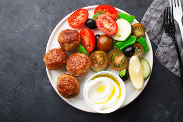 Healthy food dish. Juicy meatballs, fresh vegetables, tomatoes, cucumbers, olives, herbs, herbs with yogurt sauce with olive oil. Keto style. Top view,
