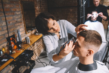 Beautiful woman hairdresser shaves the client's head with a electric trimmer in barber shop....