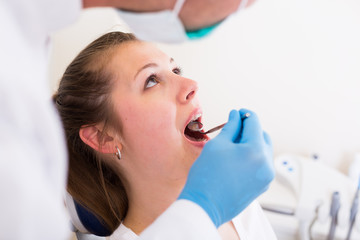 Dentist in white is taking examination of a young female