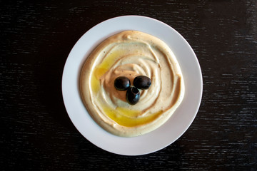 Famous traditional Arabic cuisine - dip Tahini with olives on dark wooden background. Flat lay, top view. Tahina sauce.  