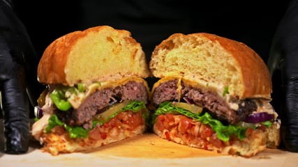 Cut craft burger is cooking on black background. Consist: red sauce salsa, lettuce, red onion, pickle, cheese, chilli green pepper, air bun and marbled meat beef. Not made ideal. Loving hand made.