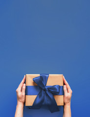 Female hands hold gift box on deep blue background with copy space for design. Caucasian girl hands...