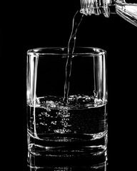 water from a bottle is poured into a glass, close-up, on a black background