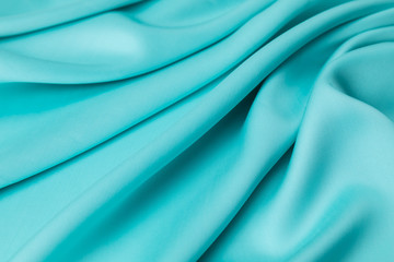 The silky streaming sateen fabric of light blue color lies on a table folds of the diagonal direction. The place for an inscription