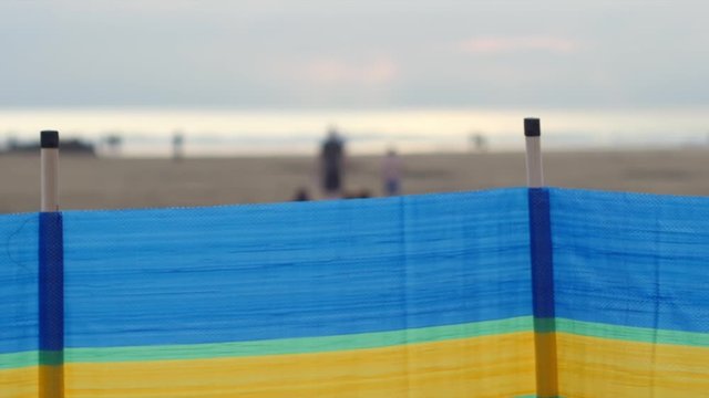 View of people on British sandy beach beyond colorful windbreak, soft focus shot