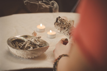 Woman hand holding herb bundle of dried sage smudge stick smoking
