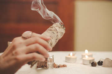 Woman hand holding herb bundle of dried sage smudge stick smoking