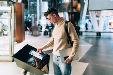 Young casual man using modern information stand in hall - obrazy, fototapety, plakaty