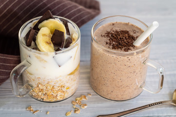 Two glass cups with ingredients banana, chocolate, oatmeal, yogurt and smoothie