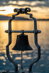 Glocke vor strahlender, leuchtender Abendstimmung und Lichtspiegelung auf Wasserfläche des...