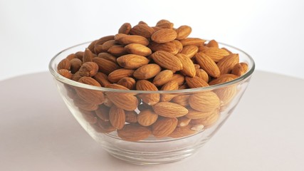 Nuts almond rotate are on a table in a plate. Snack in transparent dish on an isolated white background are spinning moving. Delicious and healthy protein-rich diet food.