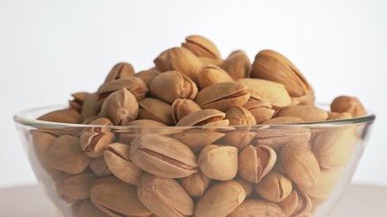 Nuts pistache rotate are on a table in a plate. Snack in transparent dish on an isolated white background are spinning moving. Delicious and healthy protein-rich diet food.