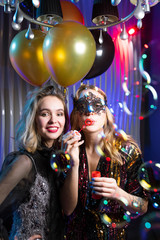 Pretty girl in lace venetian mask blowing soap bubbles with her friend near by