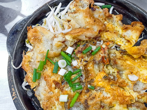 Crispy fried oyster pancake in hot plate . Oyster omelette or Fried clams . Thai food in hot pan with crispy flour and egg Popular manu Thai Cuisine. Delicious food on the sidewalk.